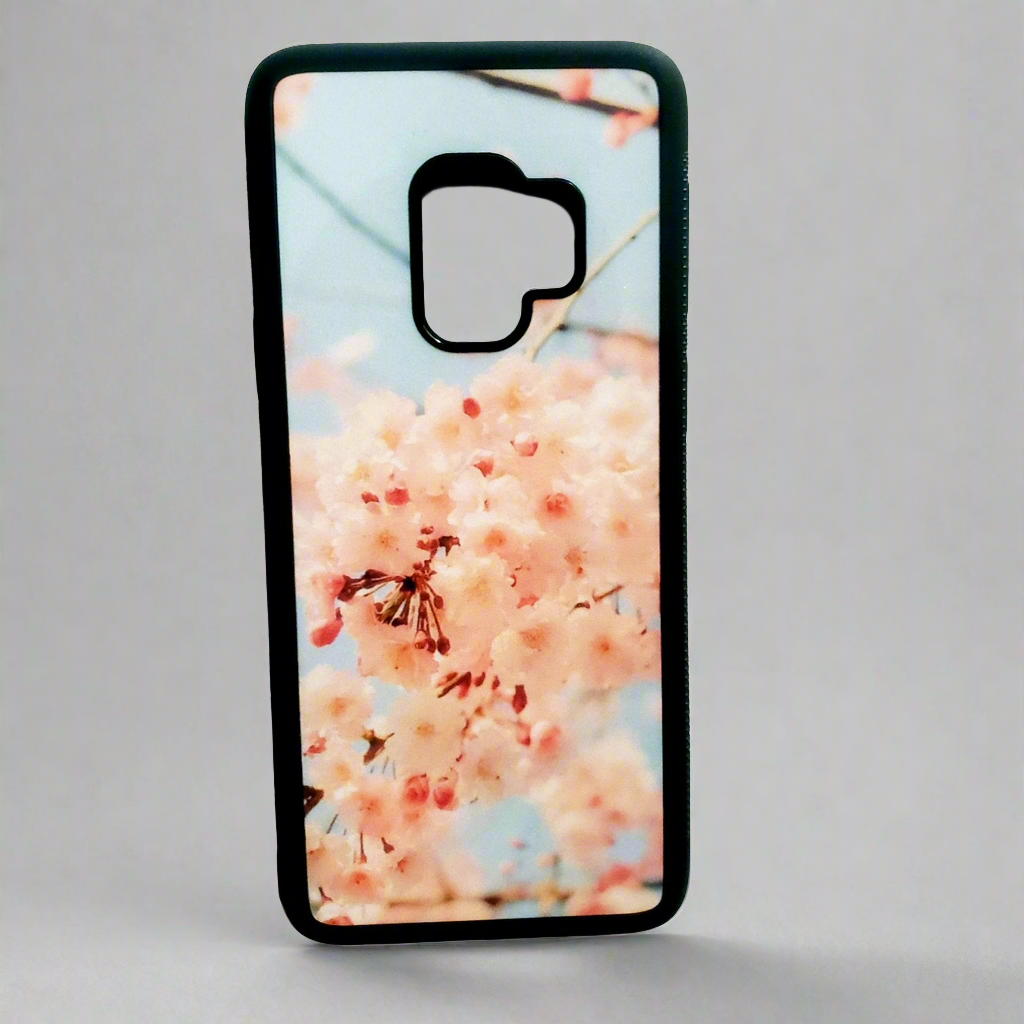 A smartphone case with a picture of peach cherry blossoms sits upright against a neutral backdrop.