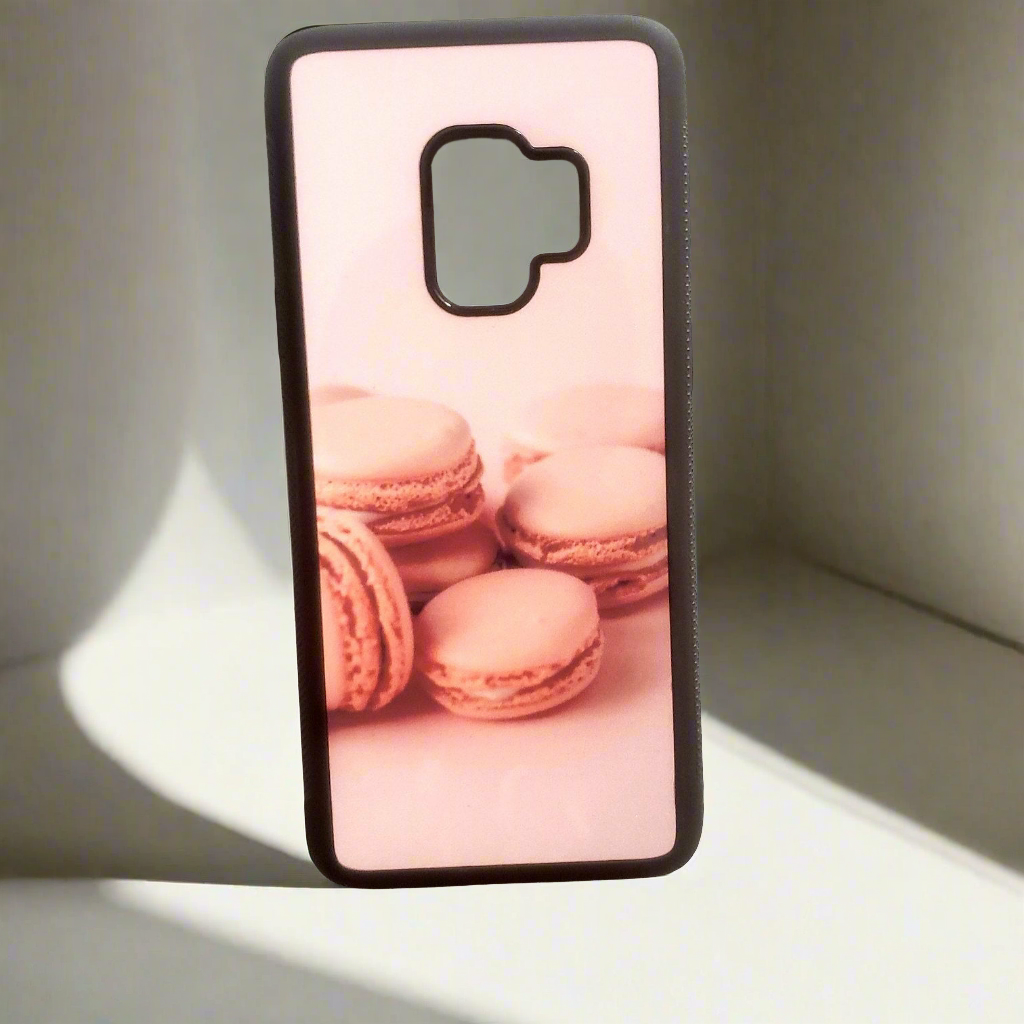  A smartphone case with a picture of pink macarons sits upright against a neutral backdrop.